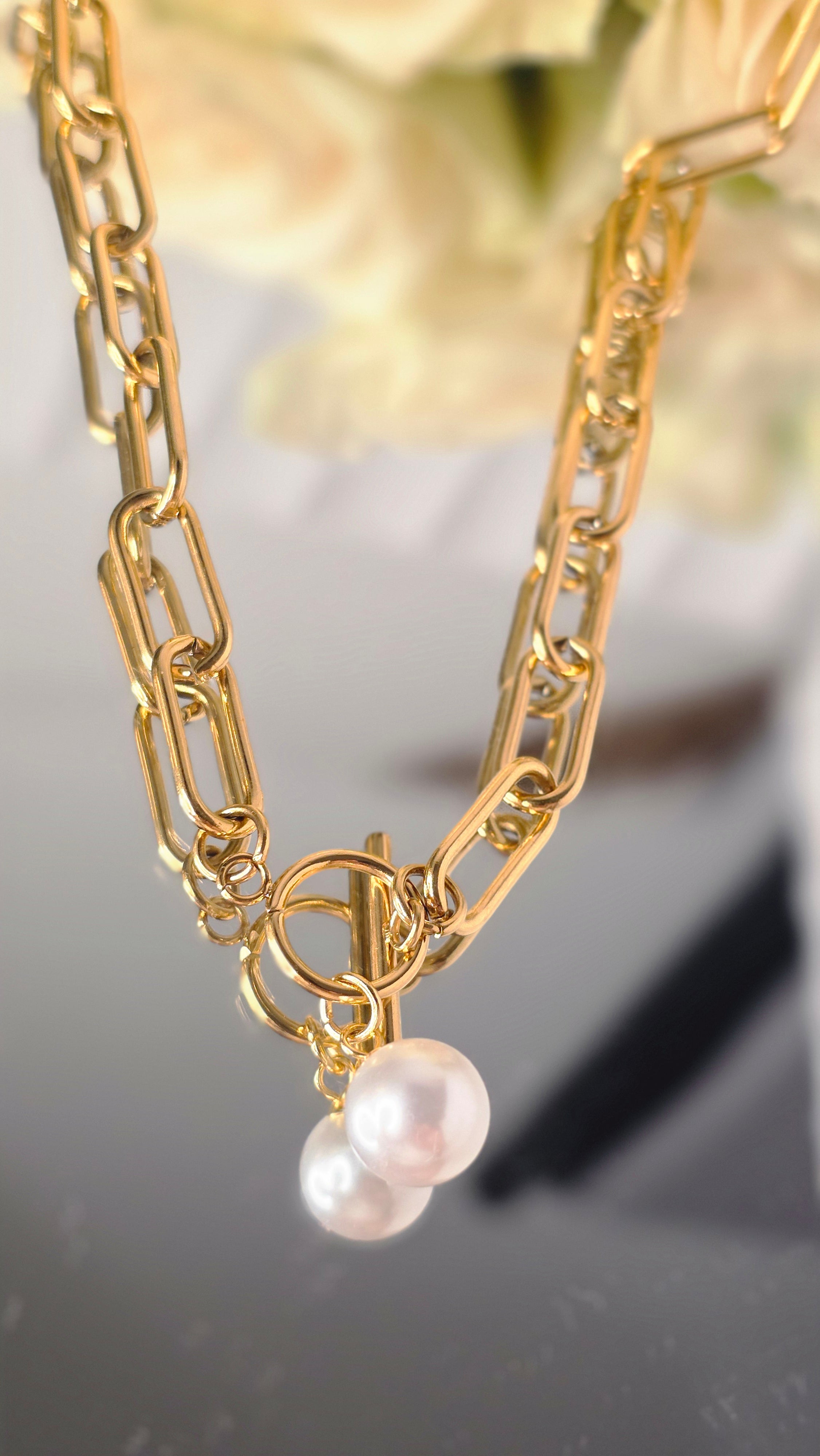 Gold chain with pearl pendants on a blurred floral background